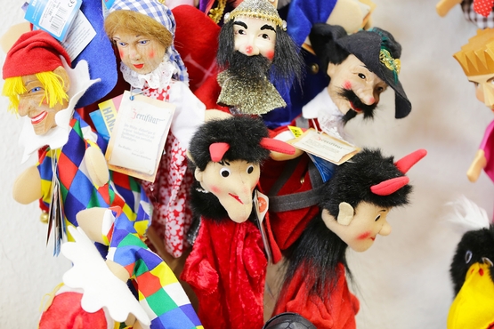 Eine Auswahl von Handpuppen in verschiedenen Ausführungen. Unter anderem sind ein Narr, ein Jäger und zwei Teufel zu sehen.