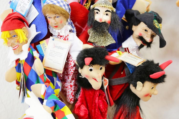 Eine Auswahl von Handpuppen in verschiedenen Ausführungen. Unter anderem sind ein Narr, ein Jäger und zwei Teufel zu sehen.